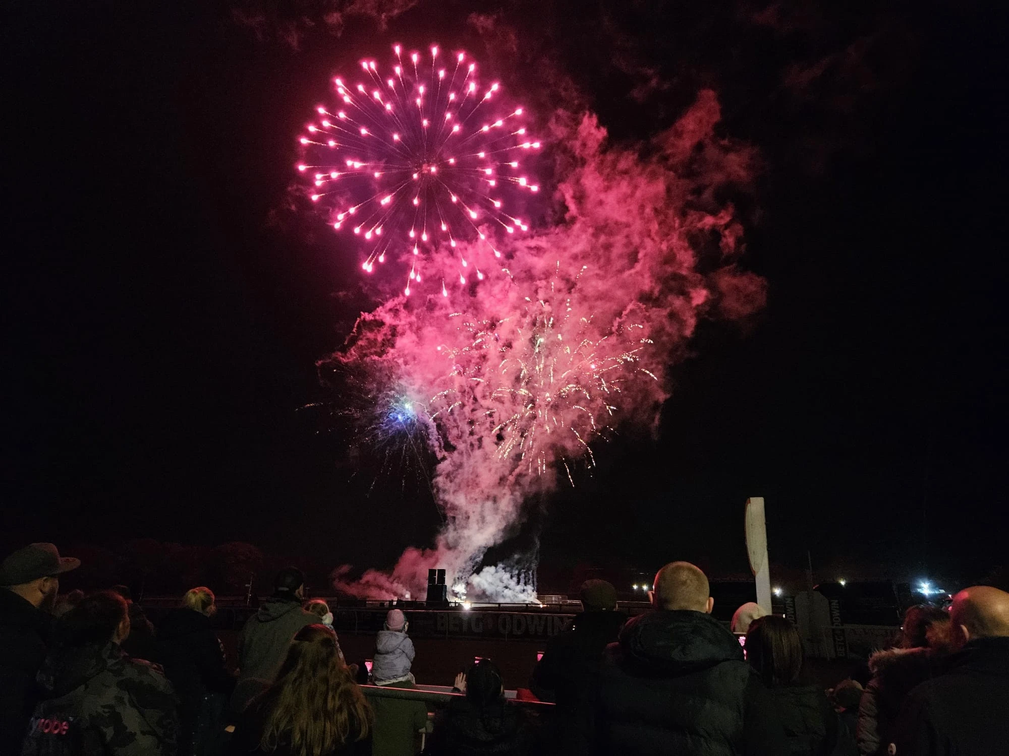 A vibrant fireworks display illuminates the night sky, with spectators watching in awe against a dark background.